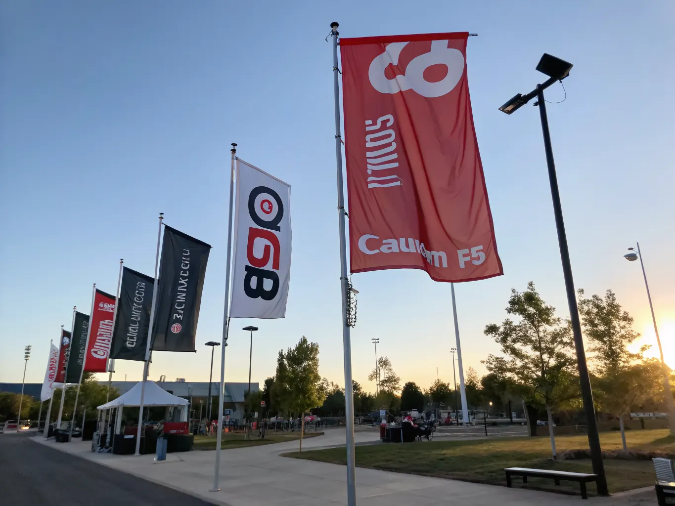 Custom sized branded flags in various dimensions mounted on poles at an outdoor corporate event campus with full-color graphics